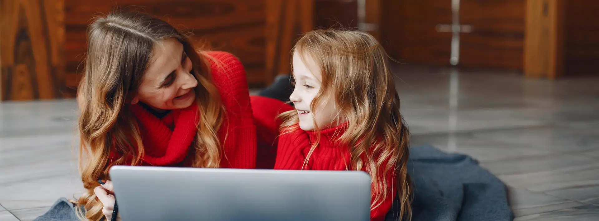 Anyuka gyermekével a szőnyegen mosolyogva laptopozik